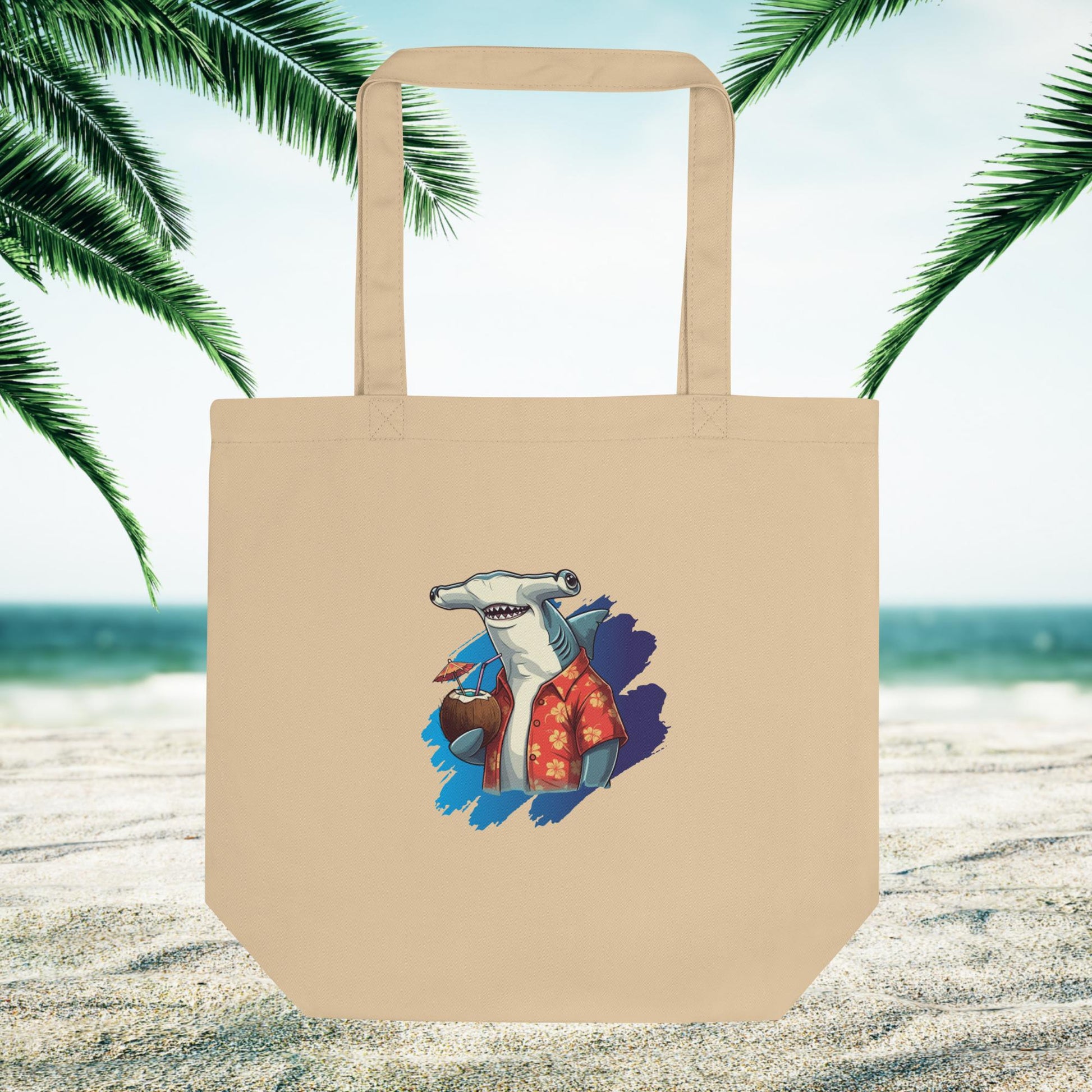 beige eco friendly tote bag with a hammerhead shark logo on a sandy beach